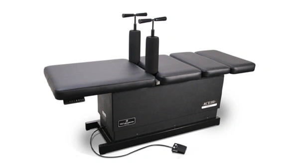 Chiropractic adjustment table with padded sections, vertical handles, and foot pedal for height adjustment.